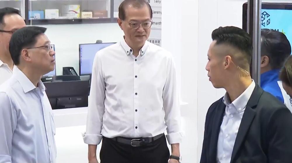 李家超參觀商場內的「藥健同心香港聖公會社區藥房」,聽取職員介紹運作情況。(電視截圖)