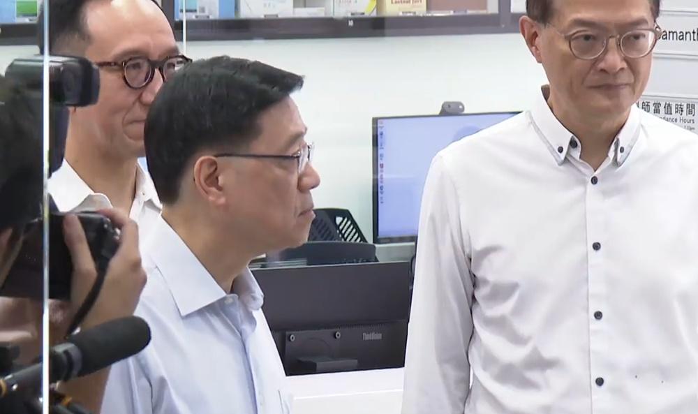 李家超參觀商場內的「藥健同心香港聖公會社區藥房」,聽取職員介紹運作情況。(電視截圖)
