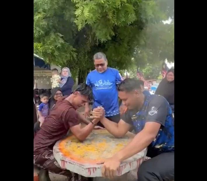 青年與大隻佬拗手瓜,試著壓倒對方。(互聯網)