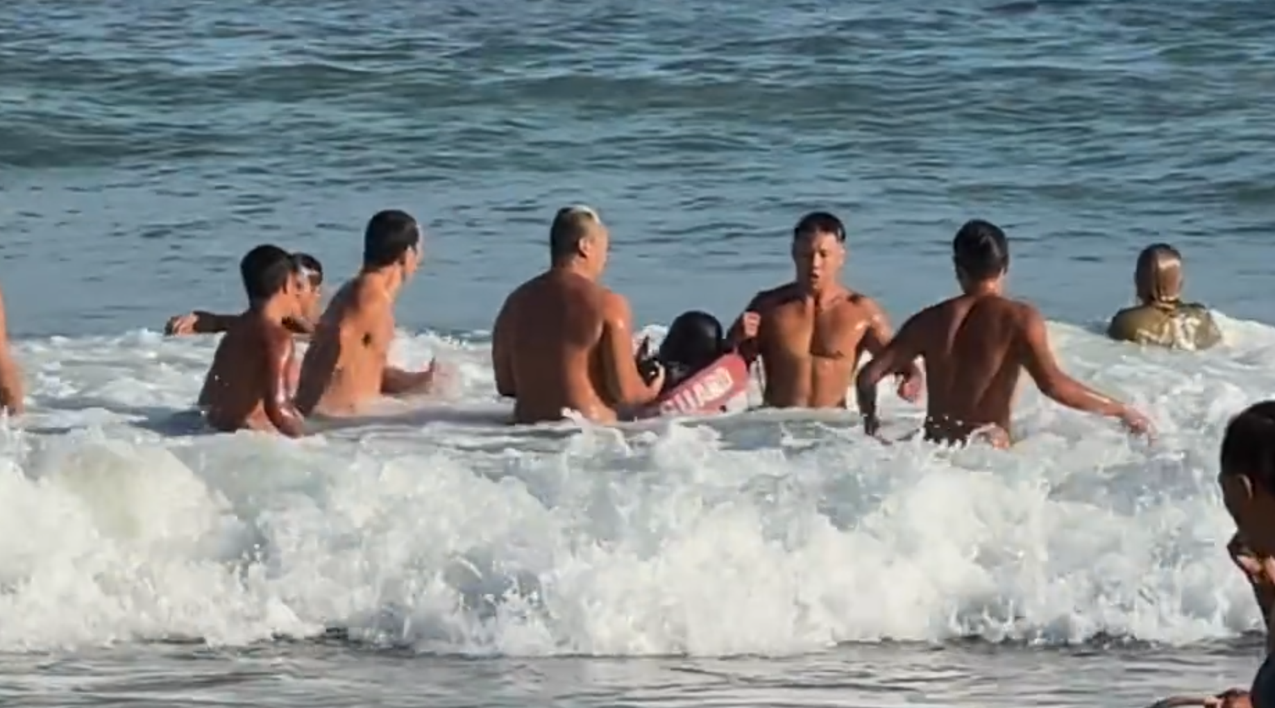 救生員游到男生身邊後將他圍著,為他套上救生浮標及示意拉繩,將男生救回上岸,期間眾人不時被大浪拍打