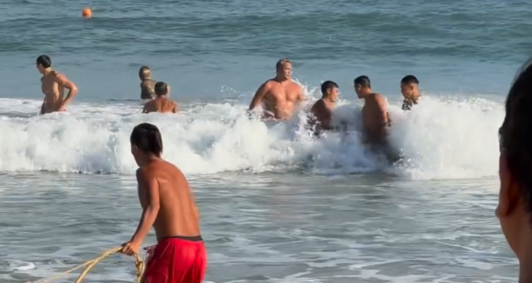 救生員游到男生身邊後將他圍著,為他套上救生浮標及示意拉繩,將男生救回上岸,期間眾人不時被大浪拍打