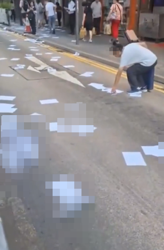 網上流傳影片,上環德輔道中近急庇利街的馬路邊散落數十張夾著10元紙幣的追債單張,不少途人檢拾查看。(影片截圖)