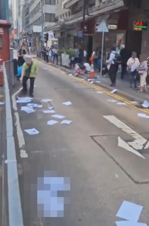 網上流傳影片,上環德輔道中近急庇利街的馬路邊散落數十張夾著10元紙幣的追債單張,不少途人檢拾查看。(影片截圖)