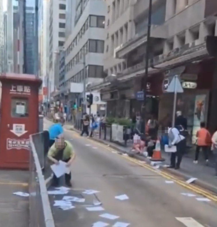 網上流傳影片,上環德輔道中近急庇利街的馬路邊散落數十張夾著10元紙幣的追債單張,不少途人檢拾查看。(影片截圖)