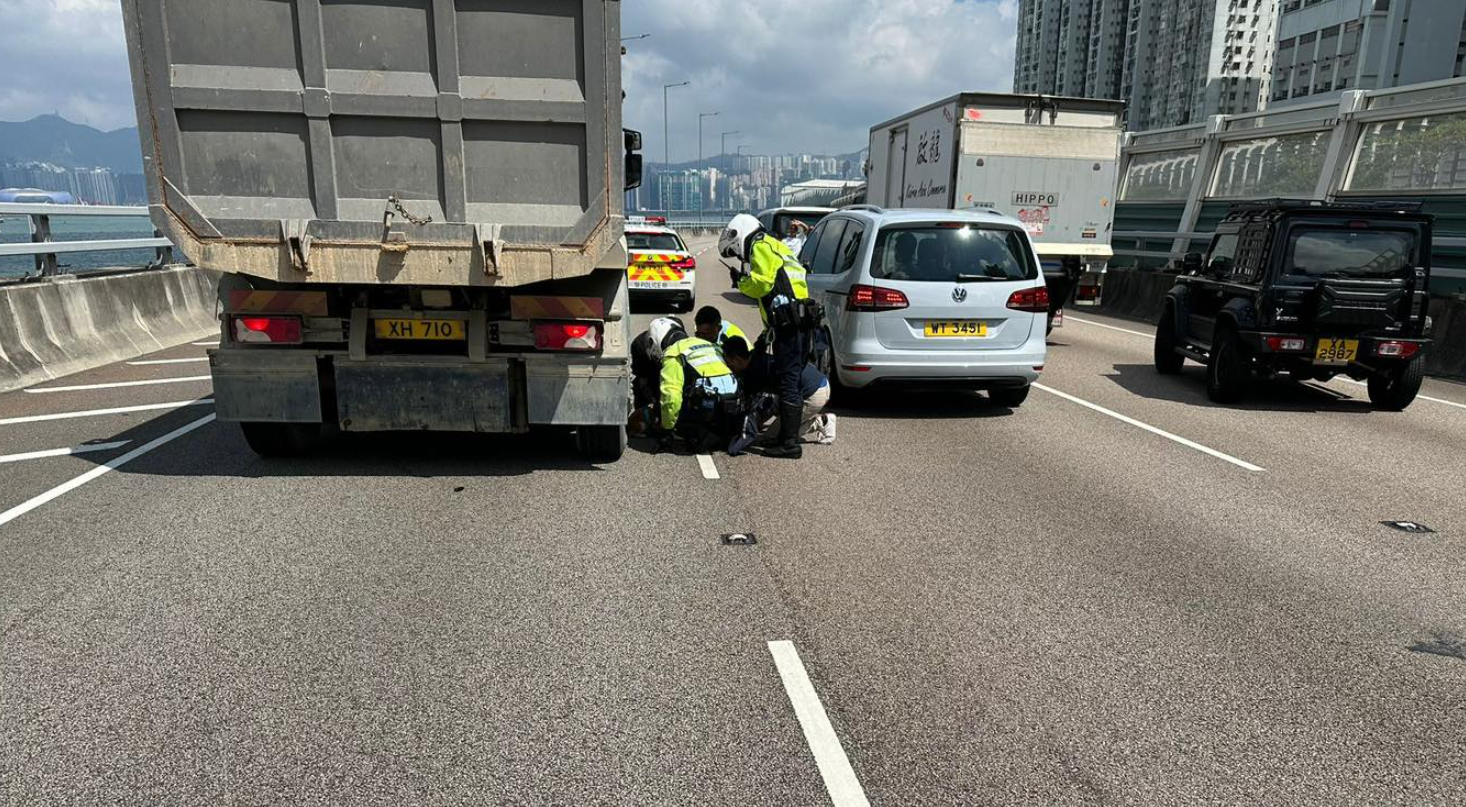 警方接報到場指示現場車輛減速,並封鎖一條行車線,最終與熱心市民合作,在泥頭車底救出柴犬。(警方圖片)