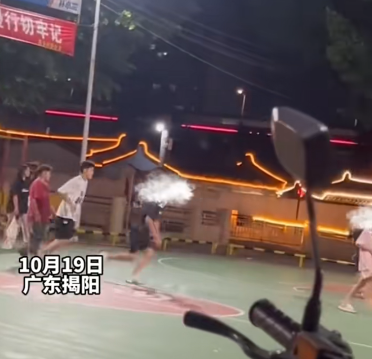 一名穿黑衣短褲的少年於籃球場急步助跑數步,飛身朝前方步行的一名穿粉色衫少女飛踢。(影片截圖)