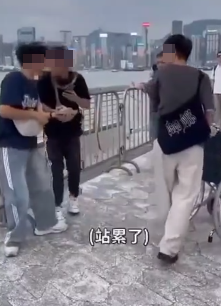 兩名香港網紅稱對很多遊客來到「踎低」感到不解,嘲諷他們是否腰骨有問題,手推輪椅往尖沙咀星光大道用普通話詢問多名蹲在地上的遊客:「我看你蹲了好久,是不是腰骨有問題,要不要坐輪椅?」(影片截圖)
