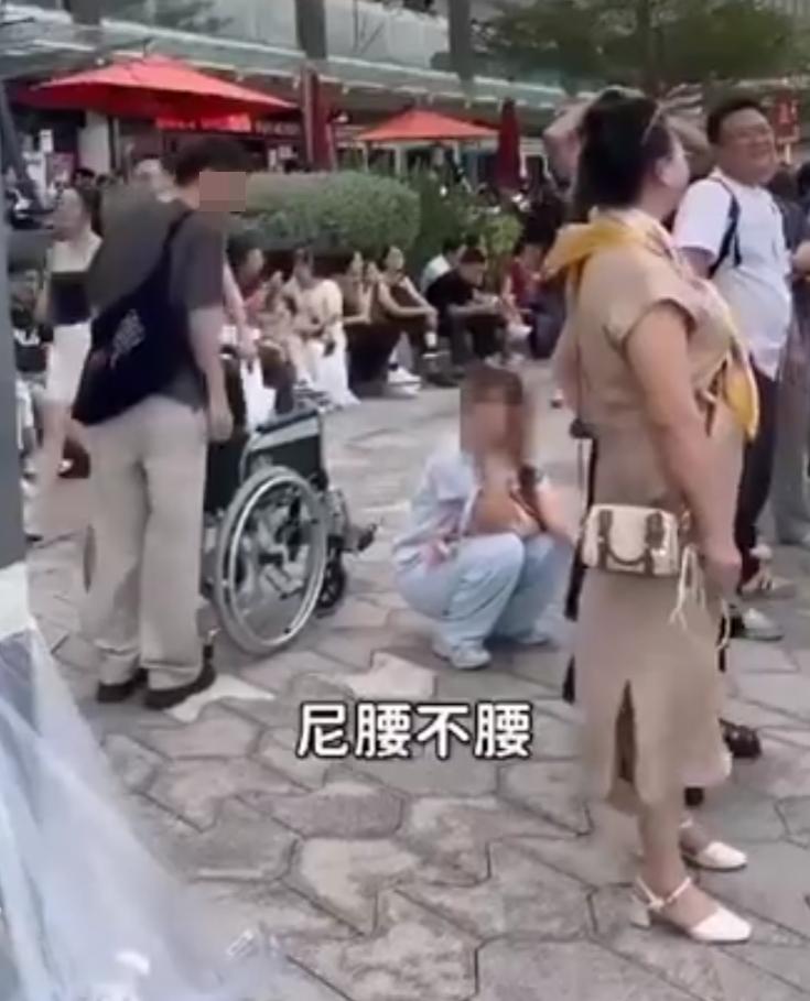 兩名香港網紅稱對很多遊客來到「踎低」感到不解,嘲諷他們是否腰骨有問題,手推輪椅往尖沙咀星光大道用普通話詢問多名蹲在地上的遊客:「我看你蹲了好久,是不是腰骨有問題,要不要坐輪椅?」(影片截圖)