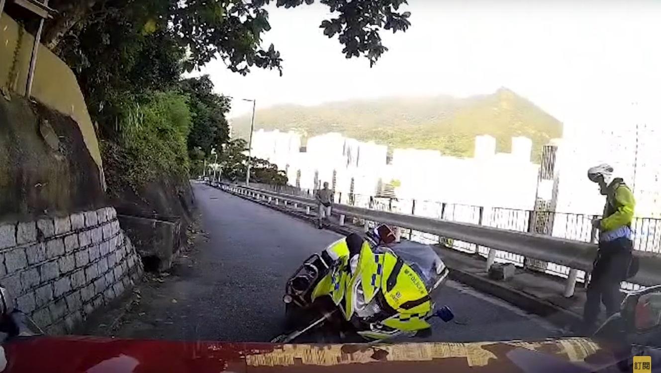 車Cam直擊︱交通警察連人帶車被撞退後,手按腰部坐在防撞欄旁待救。(網片截圖)