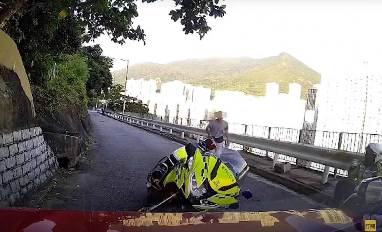 車Cam直擊︱交通警察連人帶車被撞退後,手按腰部坐在防撞欄旁待救。(網片截圖)