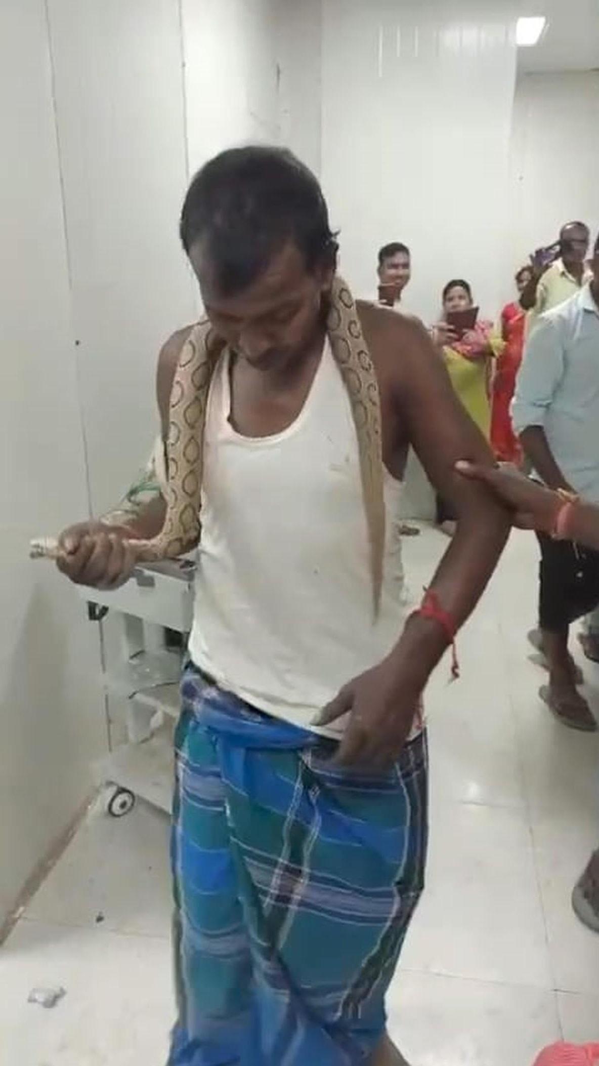 男子被咬後頸部掛著毒蛇跑進醫院求助,在場民眾驚訝,紛紛舉機拍攝。(互聯網)