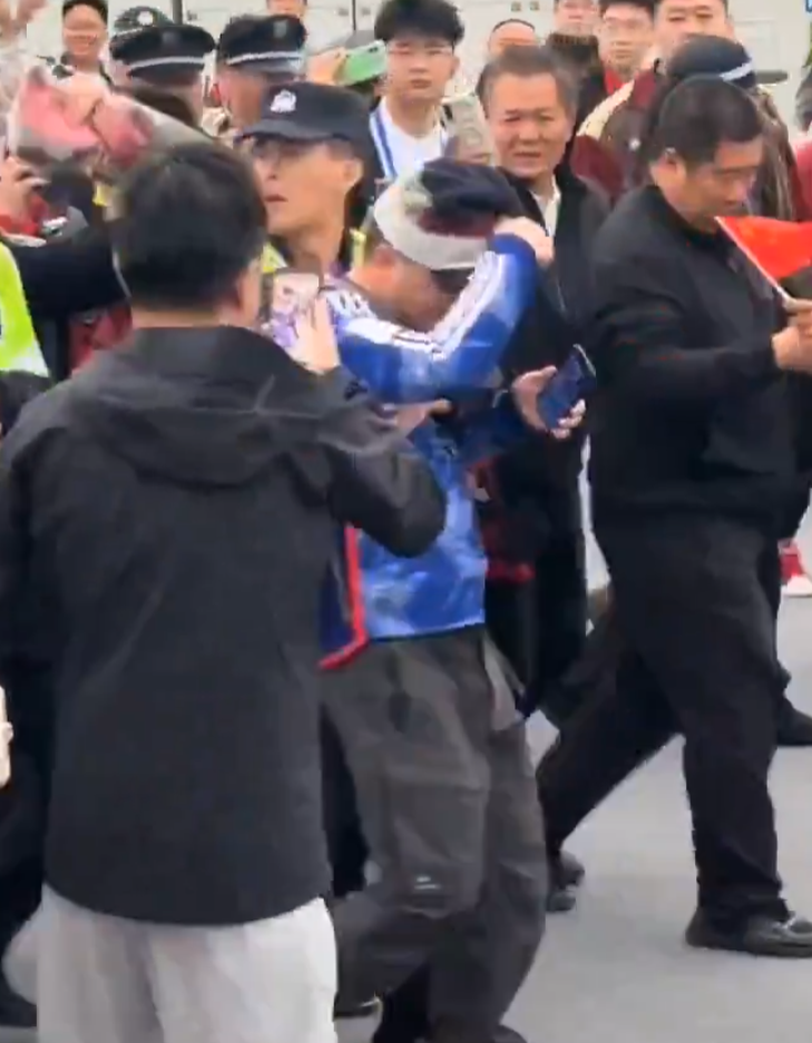 男子由多名警員護送,期間遭人扯脫帽子。(影片截圖)