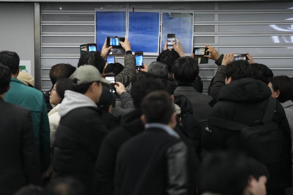 大批家屬聚集在務安機場等候消息,部分人舉機拍攝乘客名單。(美聯社)