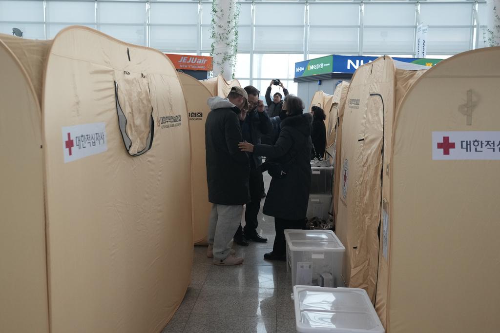 務安機場客運大樓內設置臨時帳幕,供乘客家屬休息,有家屬神情憂傷,旁人安慰。(美聯社)