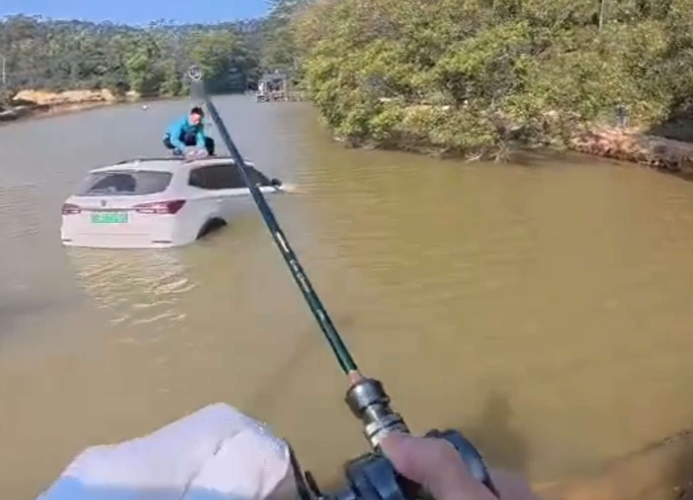 深圳有釣魚人士遇到一輛車墮湖,車主站在車頂處境危險。於是他伸出魚桿向車頂抛出魚絲,借助風力和水的浮力,將車輛「釣回」拉到岸邊。(影片截圖)