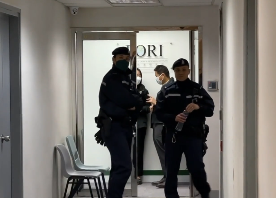 鍾庭耀被國安處人員帶到位於黃竹坑的香港民研辦公室,警員在門外駐守。(有線新聞畫面)
