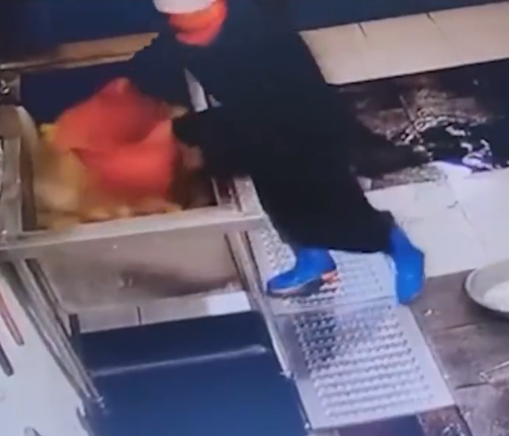 江西新余市第十六中學食堂有一名戴廚師帽的員工用腳多次踩踏水桶內的食材,當時他還穿著水靴。(影片截圖)