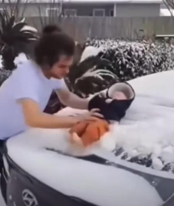 美國德州一名男子,以3個月嬰兒的身體除去車上的積雪。(網上截圖)