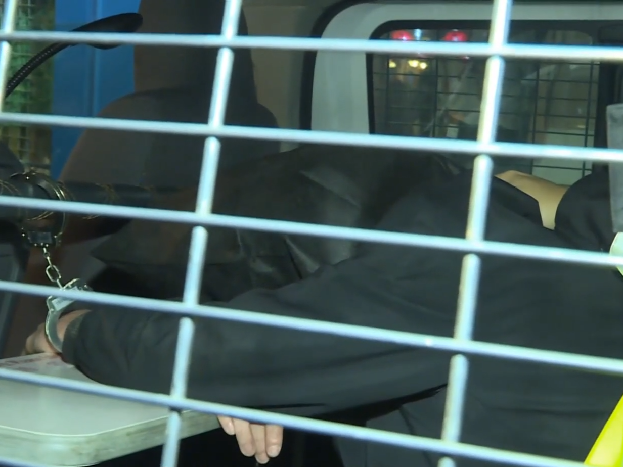 被捕男子黑布蒙頭,鎖上手銬,在警車上協助調查。(有線新聞截圖)