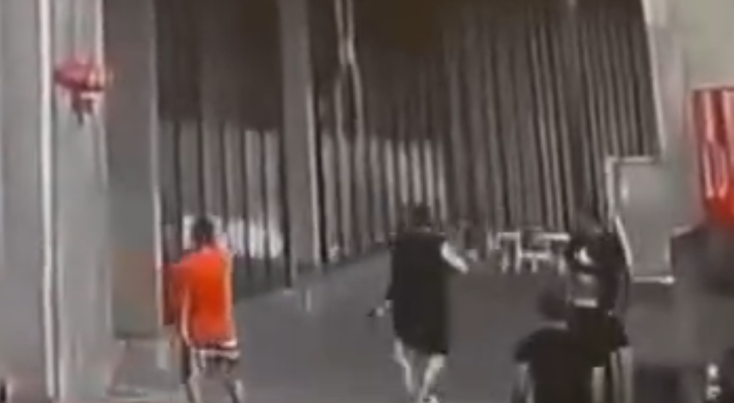 影片顯示,有兩名男子拿著兩支步槍跳下車衝進樓內,另有一名男子手持一把短槍對準一輛汽車的後座。(影片截圖)