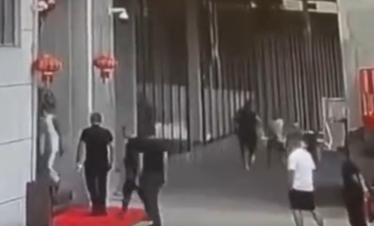 影片顯示,有兩名男子拿著兩支步槍跳下車衝進樓內,另有一名男子手持一把短槍對準一輛汽車的後座。(影片截圖)