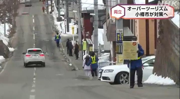 北海道小樽市街上有穿螢光背心的保安員巡邏並舉牌,防止遊客衝出馬路拍攝。(互聯網)