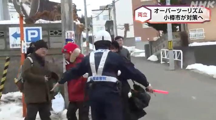 北海道小樽市有遊客在街上拍攝,保安員維持秩序,指示遊客不要走出馬路。(互聯網)