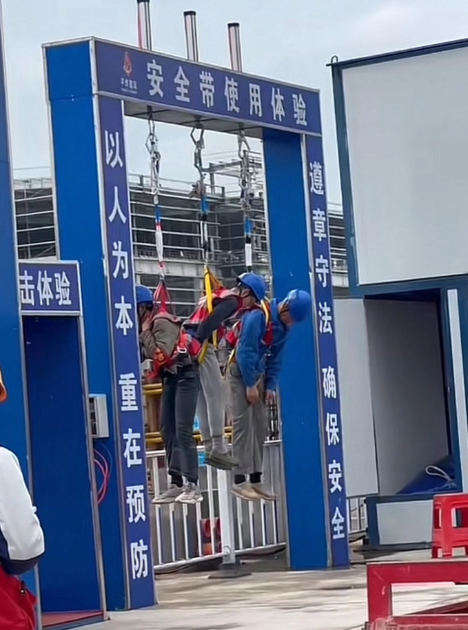 四川宜賓市一處地盤門口,3名工人疑因高空工作時未配戴安全帶,被吊掛在安全帶使用體驗區「示眾」懲罰。(影片截圖)
