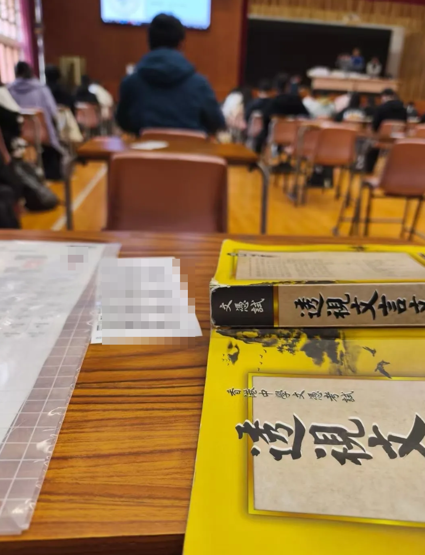 另一幅在Threads流傳照片,拍攝到考場及其他考生,枱面放有電腦條碼貼紙、中文試12篇範文精讀書《透視文言文》、疑似貼有個人照片的准考證。發帖者指,有應屆考生疑將該相片上傳至微信,相信事發日期為4月2日應考中文科卷一期間於東華三院邱子田紀念中學發生。