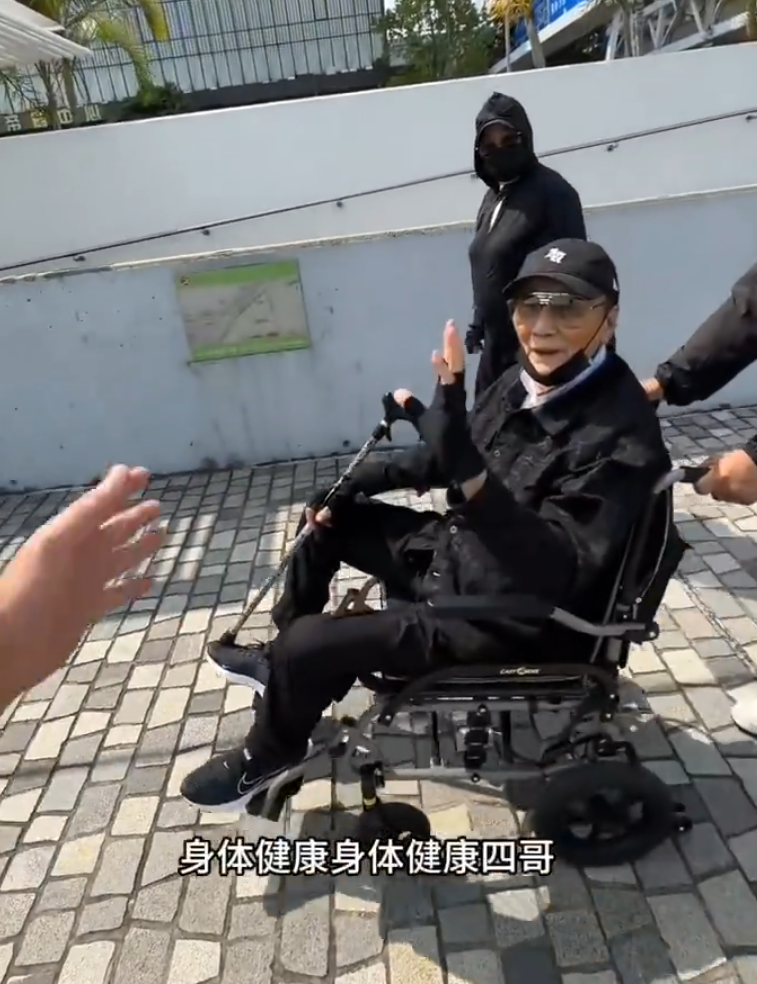 片中的謝賢戴上黑色Cap帽、黑超,又以全黑造型坐在輪椅上於尖沙咀散步,身邊有兩位同樣以全黑打扮的人在身旁陪伴及照顧他(影片截圖)