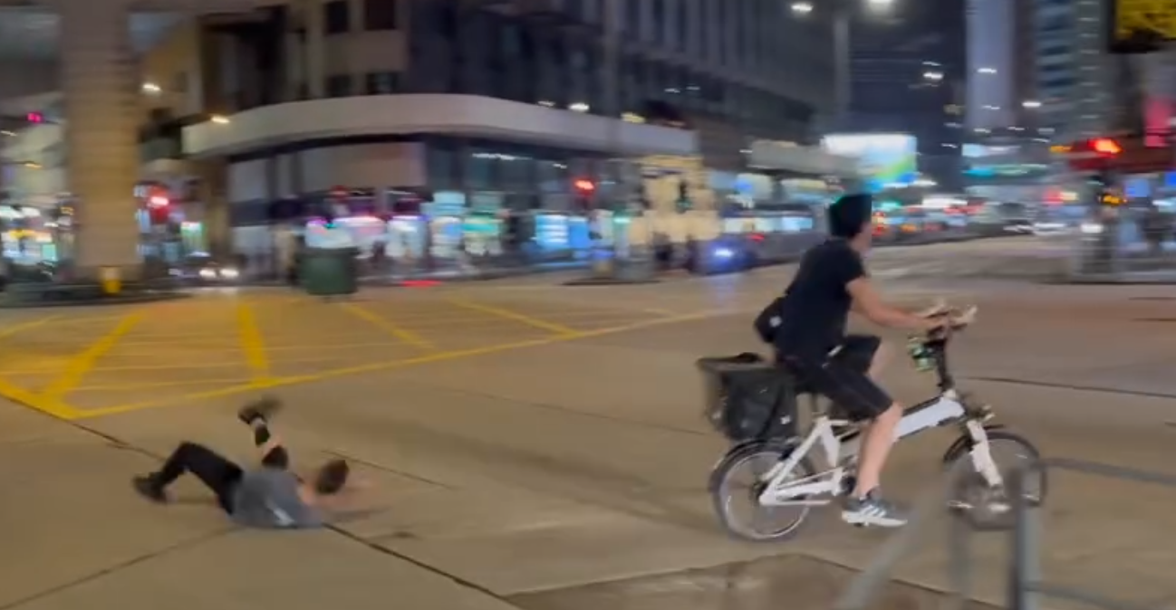 一名的士司機離開其座駕,在馬路上追趕一名騎單車的男子,期間的士司機撲前意圖捉住單車惟失手撲空,整個人如滾地葫蘆向前倒地。(Threads)