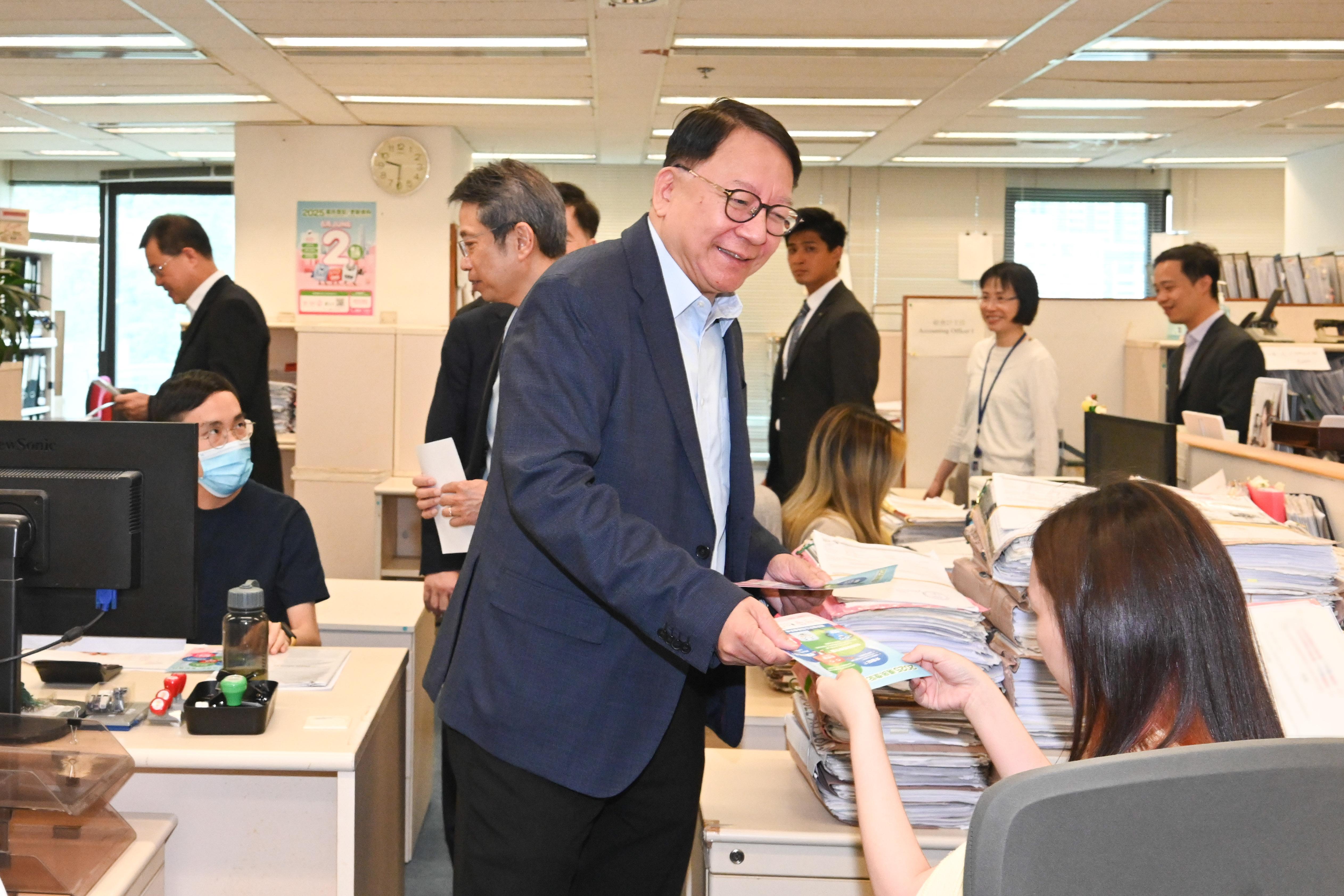 圖示陳國基(中)在法律援助署同事的工作間向他們派發宣傳單張。(政府新聞處)