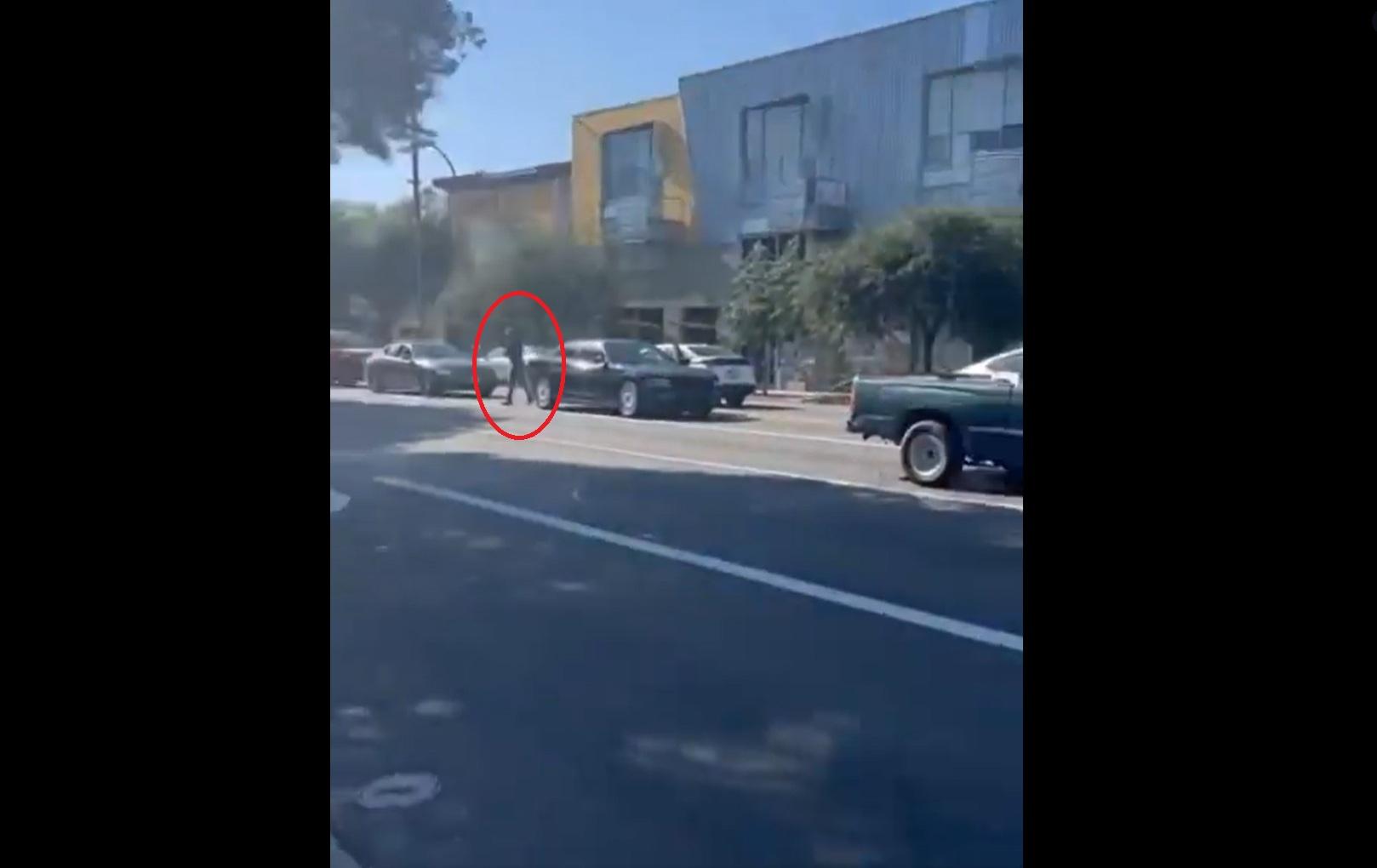 本月18日在加州帕薩迪納(Pasadena),一名疑似ICE男探員(紅圈)下車,拿槍指嚇在馬路另一邊拍攝的民眾。(互聯網)