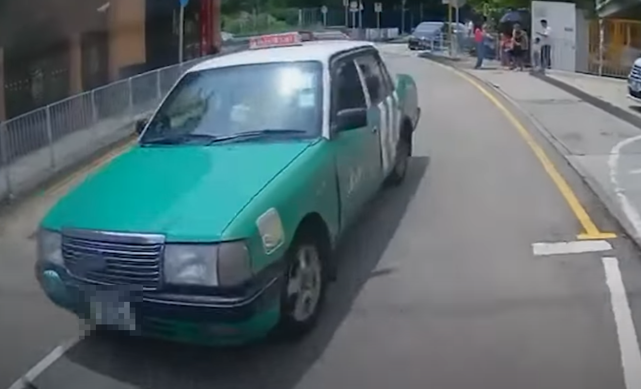 一輛綠色的士在屯門掃管笏管青路斑馬線過路處前,越過雙白線抽頭超越Cam主車輛,再逆線駛過斑馬線,一對母子過路走至一半時及時停下。(影片截圖)