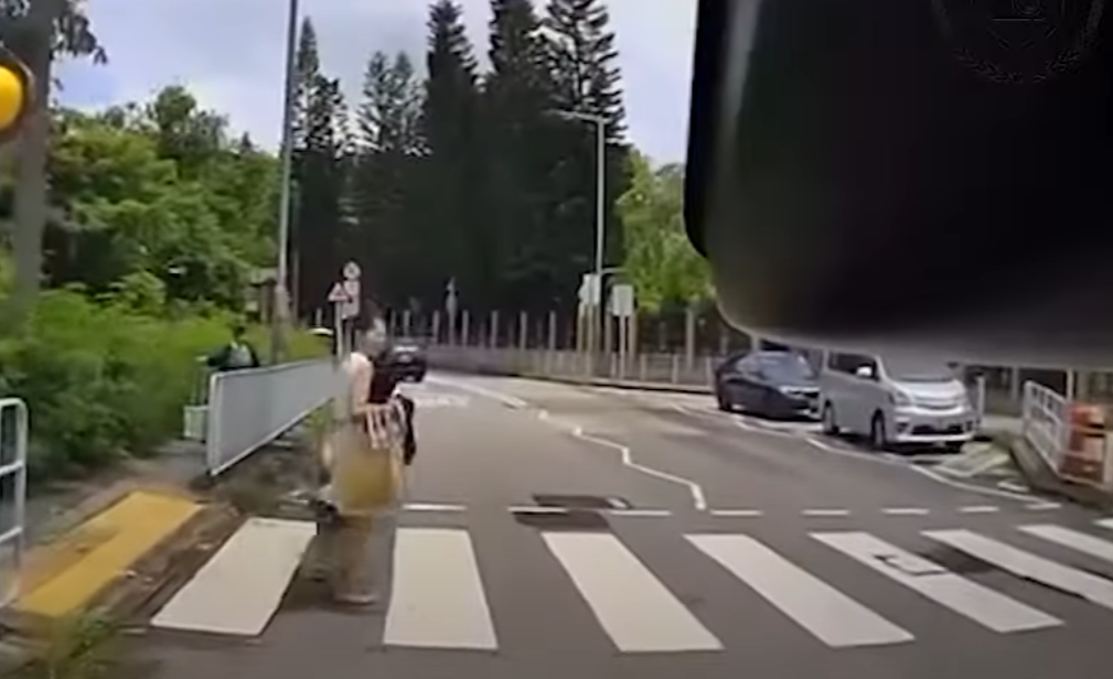 一輛綠色的士在屯門掃管笏管青路斑馬線過路處前,越過雙白線抽頭超越Cam主車輛,再逆線駛過斑馬線,一對母子過路走至一半時及時停下。(影片截圖)