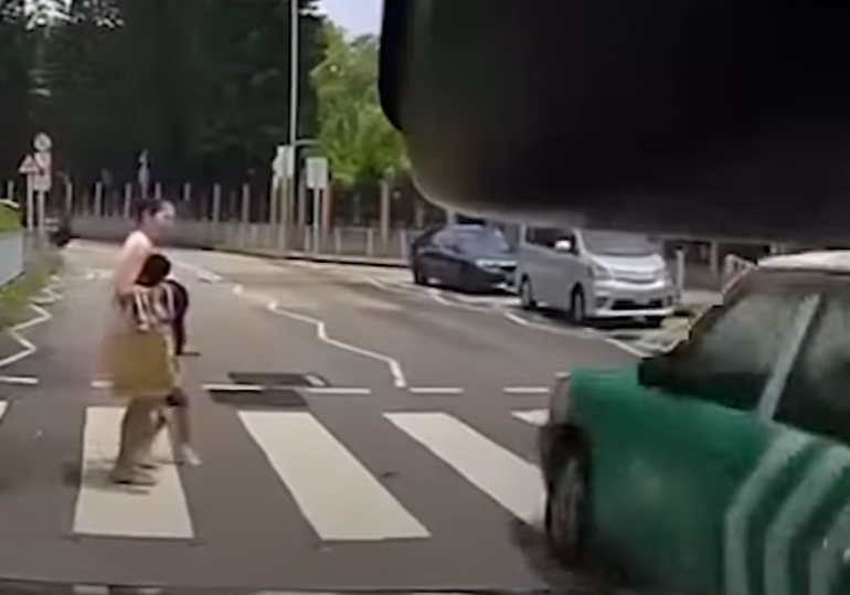 一輛綠色的士在屯門掃管笏管青路斑馬線過路處前,越過雙白線抽頭超越Cam主車輛,再逆線駛過斑馬線,一對母子過路走至一半時及時停下。(影片截圖)