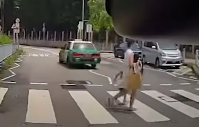 一輛綠色的士在屯門掃管笏管青路斑馬線過路處前,越過雙白線抽頭超越Cam主車輛,再逆線駛過斑馬線,一對母子過路走至一半時及時停下。(影片截圖)