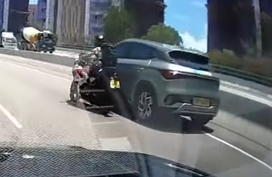 屯門公路一輛電單車往九龍方向快線行駛,至珠海學院對開時被一輛銀色私家車從後逼近,更加速強行切入電單車與路中石壆之間的狹窄空位爬頭,導致雙方擦撞險釀意外。(車cam L(香港群組)fb)