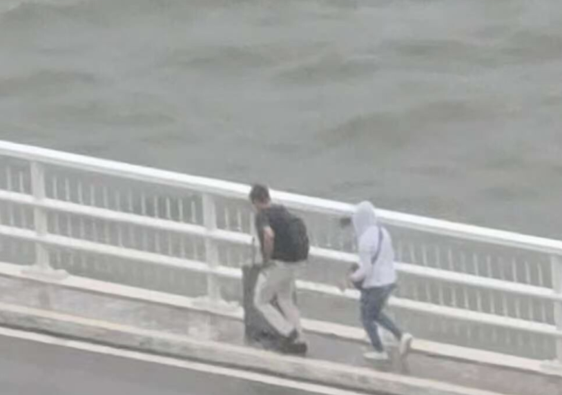 澳門兩名旅客推着行李箱,經嘉樂庇總督大橋由澳門半島行向氹仔。治安警察局接報後,協助兩人返回安全地點,由於兩人違反現場按道路交通規章相關規定設立的禁止行人通行符號,已依法被檢控。(影片截圖)