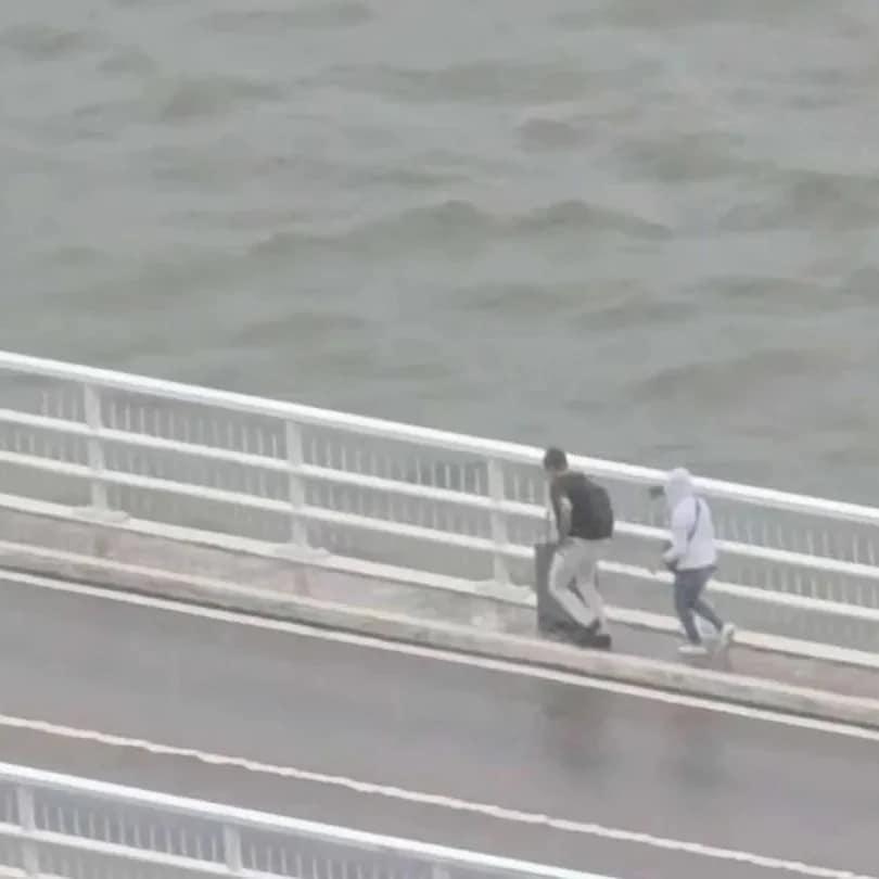 澳門兩名旅客推着行李箱,經嘉樂庇總督大橋由澳門半島行向氹仔。治安警察局接報後,協助兩人返回安全地點,由於兩人違反現場按道路交通規章相關規定設立的禁止行人通行符號,已依法被檢控。(影片截圖)