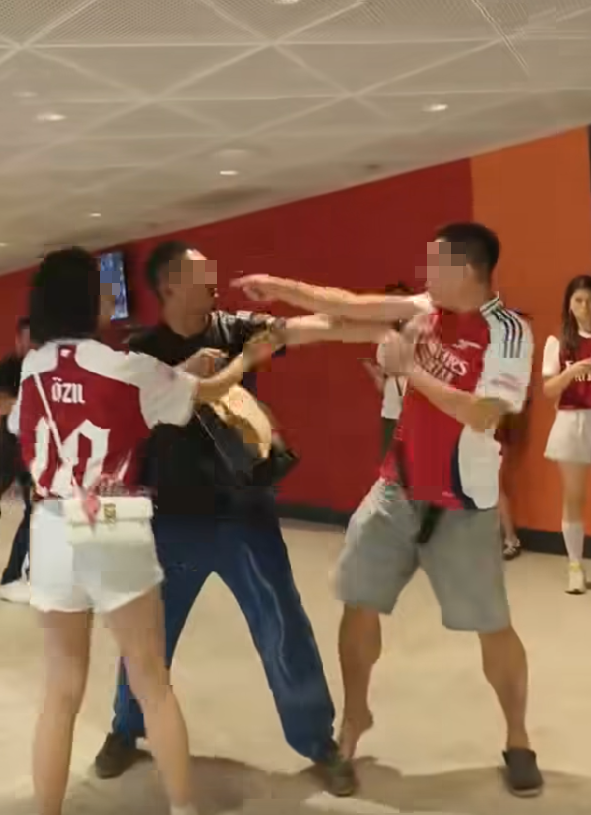 社交平台網上流傳一條影片,可見兩名分別穿上紅色及黑色阿仙奴球衣的男球迷在啟德主場館「內鬨」爭執講手,一名與黑衫男同行的女伴嘗試勸交,惟被誤打到口部。(影片截圖)