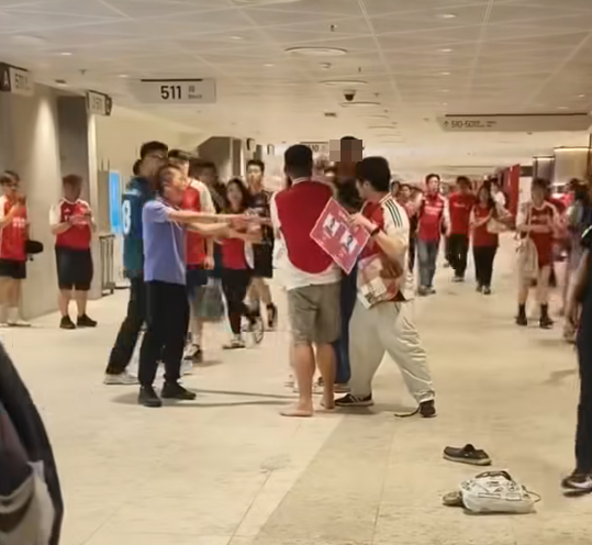 社交平台網上流傳一條影片,可見兩名分別穿上紅色及黑色阿仙奴球衣的男球迷在啟德主場館「內鬨」爭執講手,一名與黑衫男同行的女伴嘗試勸交,惟被誤打到口部。(影片截圖)