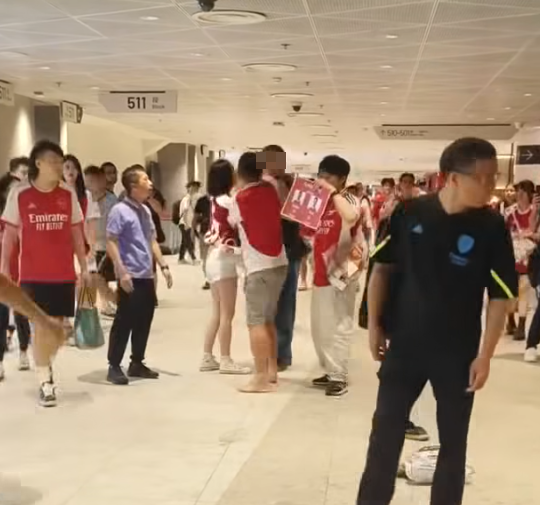 社交平台網上流傳一條影片,可見兩名分別穿上紅色及黑色阿仙奴球衣的男球迷在啟德主場館「內鬨」爭執講手,一名與黑衫男同行的女伴嘗試勸交,惟被誤打到口部。(影片截圖)