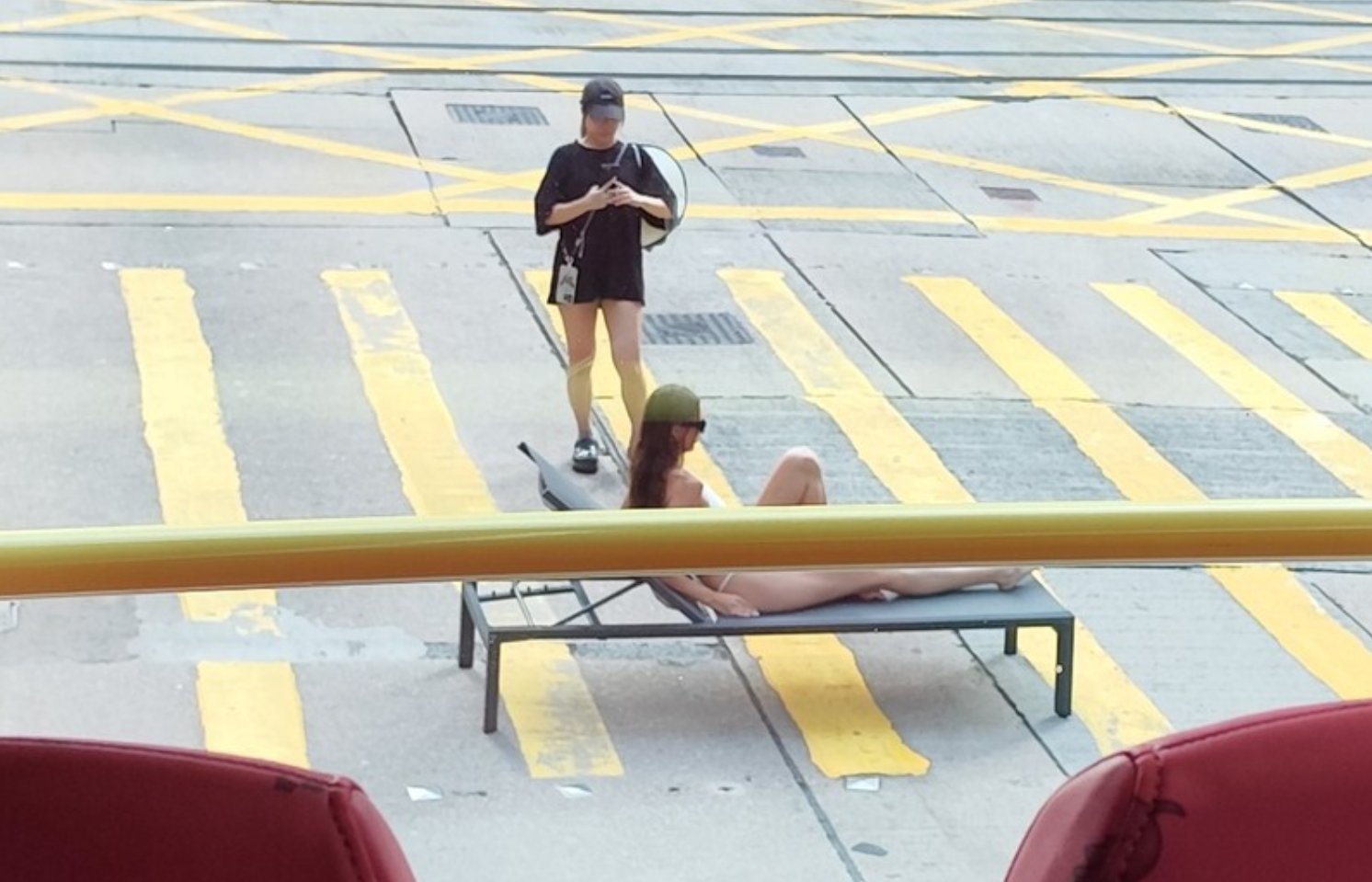 有網民拍得照片,可見位於中環畢打街連接德輔道中的繁忙馬路班馬線上,一名身穿白色三點式泳衣的長髮女子在坐沙灘椅「曬太陽」,引起車上乘客側目拍下「奇景」。(Threads)