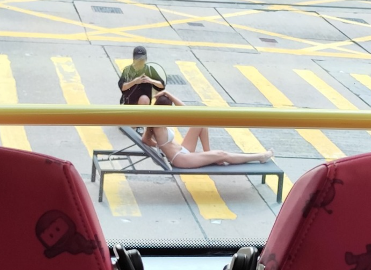 有網民拍得照片,可見位於中環畢打街連接德輔道中的繁忙馬路班馬線上,一名身穿白色三點式泳衣的長髮女子在坐沙灘椅「曬太陽」,引起車上乘客側目拍下「奇景」。(Threads)