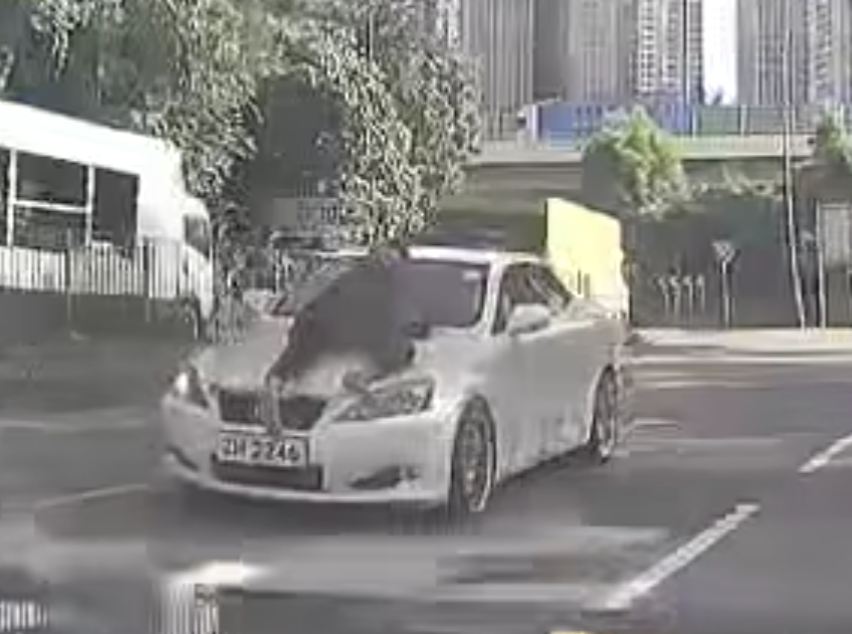 片段中一輛白色私家車沿粉錦公路行駛,一名穿黑衣的人伏在該車頭上(影片截圖)