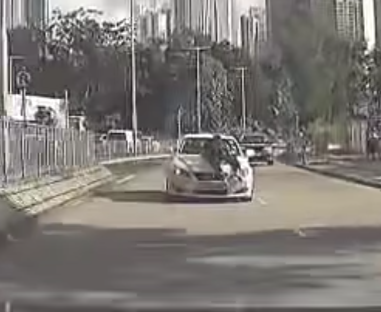 片段中一輛白色私家車沿粉錦公路行駛,一名穿黑衣的人伏在該車頭上(影片截圖)
