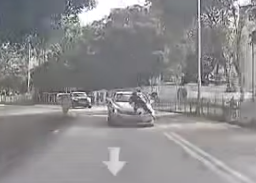 片段中一輛白色私家車沿粉錦公路行駛,一名穿黑衣的人伏在該車頭上(影片截圖)