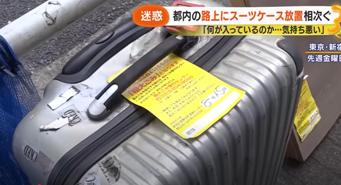 日本媒體報道,有人在東京新宿街上丟棄舊行李箱,工作人員在上面貼標籤,呼籲物主認領。(互聯網)