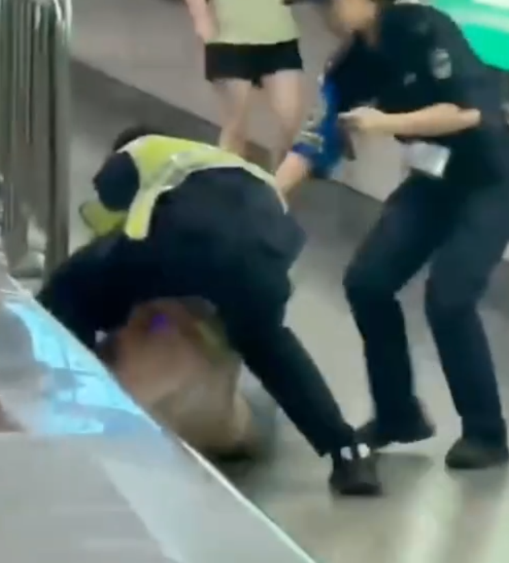 深圳地鐵女乘客以拳頭及手袋激烈追打一名的男安檢員,男方僅用手阻擋及後退,其後另外一名女安檢員上前制止,亦被女乘客用手袋重擊頭部。男安檢員隨即反手擒拿將女乘客制服,隨後女乘客躺臥在地不動。(影片截圖)